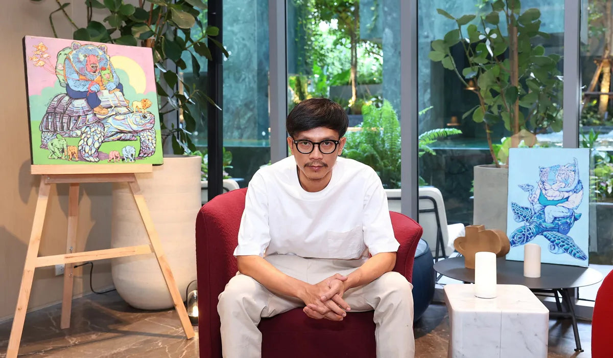 Bangkok artist Bonus TMC sitting in a modern room with colorful artworks on easels.