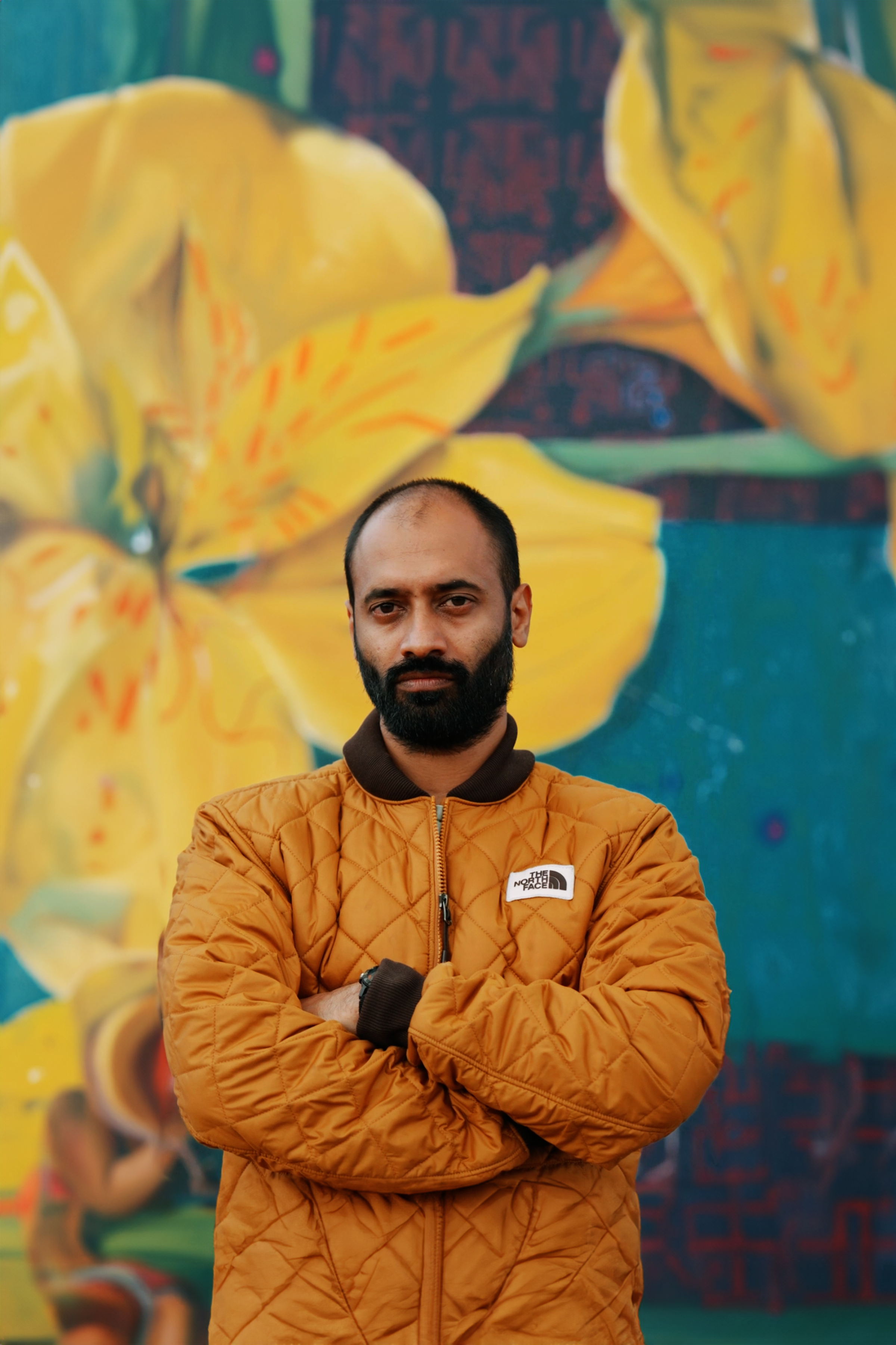 Artist WiseTwo stood in front of a beautiful yellow floral mural in Nairobi